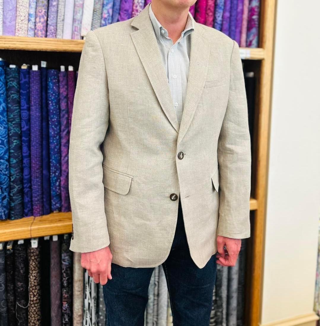 The finished linen jacket worn and buttoned, in front of shelves of fabric.