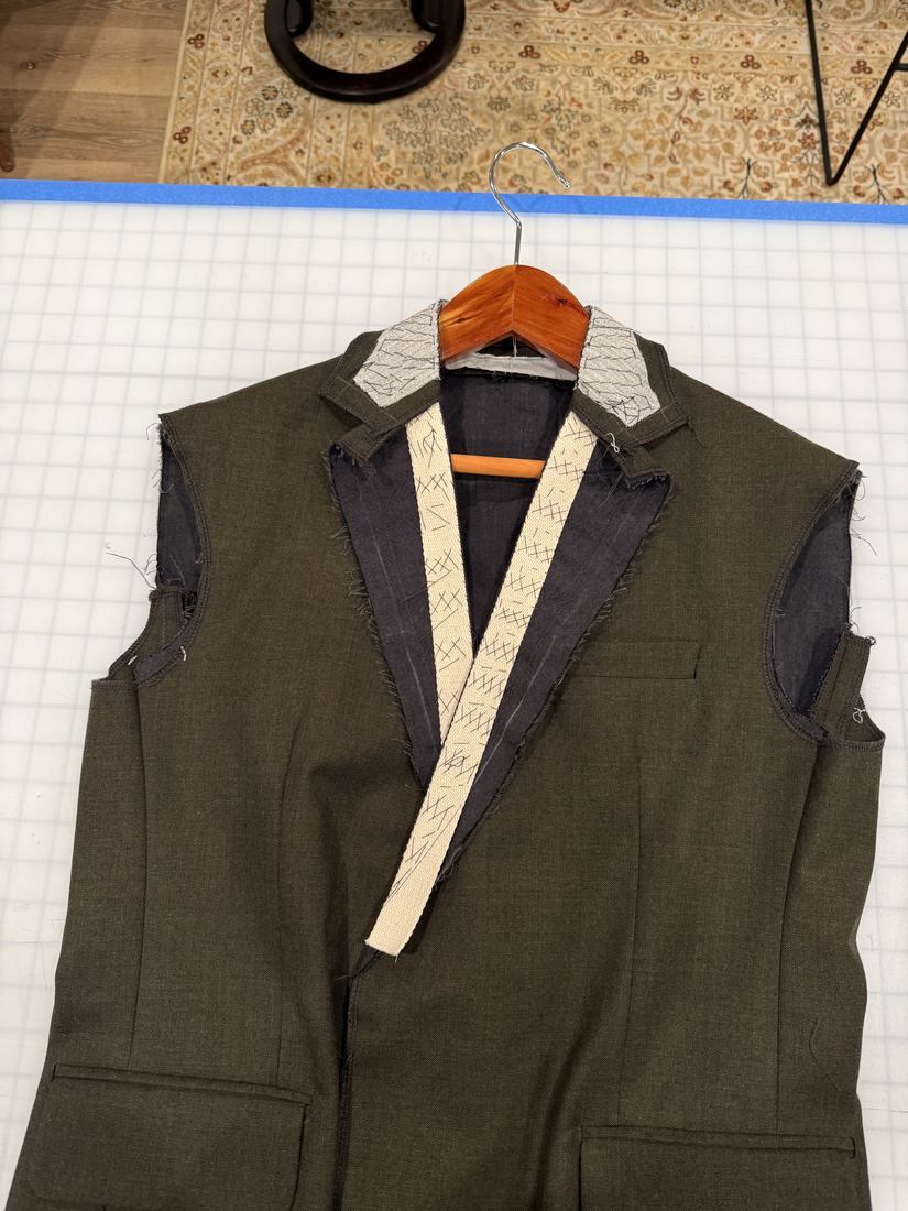 Jacket shell on a hanger with the collar attached and lapels taped.