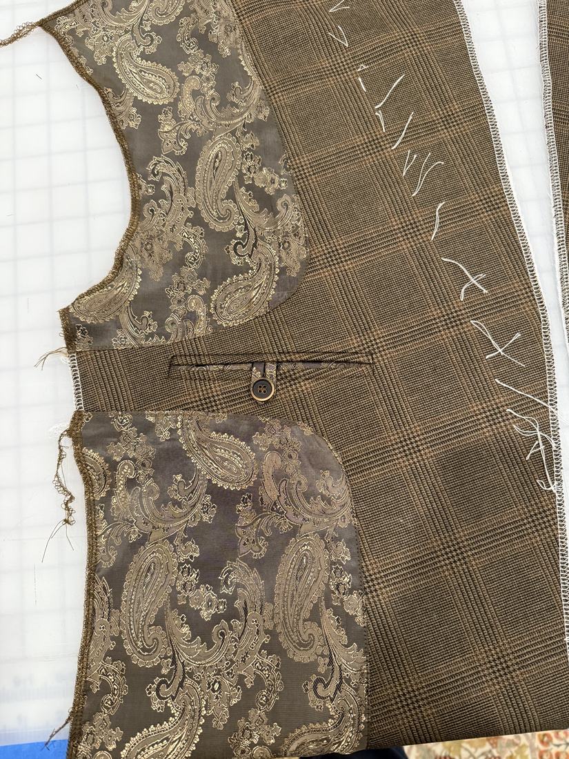 A jacket front laid flat: glen plaid wool with a gold brocade facing and a finished welt pocket.